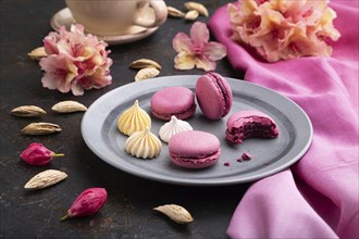 Purple macarons or macaroons cakes with cup of coffee on a black concrete background and pink