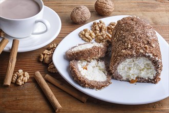 Roll cake with curd and walnuts isolated on brown wooden background, close up