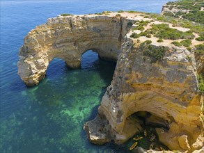 Large rock formations with natural arches on the coast, near water with canoes, aerial view, Praia