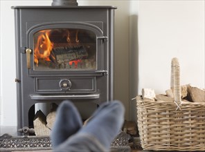 Roaring domestic household wood burning ClearView stove fire log basket with feet up in foreground