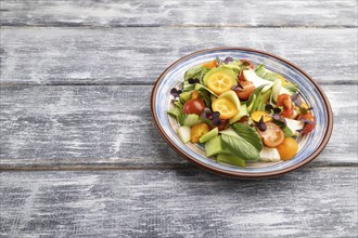 Vegetarian salad of pac choi cabbage, kiwi, tomatoes, kumquat, microgreen sprouts on gray wooden