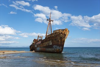 A rusty ship hull with graffiti lies abandoned against a vivid blue sky on the seashore, shipwreck