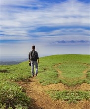 View of backpacker man walking on the beautiful hill. Backpacker walking on a beautiful hill