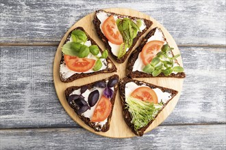 Grain rye bread sandwiches with cream cheese, tomatoes and microgreen on gray wooden background.