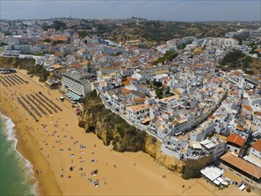 City on a hill with a lively sandy beach on the coast and numerous buildings, aerial view,