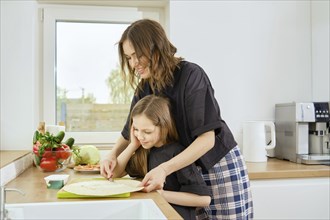 Mother and daughter spread cream cheese on a flatbread together while standing in a bright kitchen