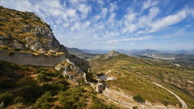 A view over a winding mountain path leading to ancient ruins with a sweeping vista, Archaic Castle,