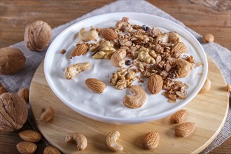 White plate with greek yogurt, granola, almond, cashew, walnuts on brown wooden background. close