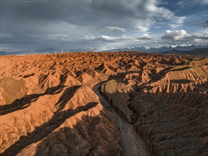 River bed runs through a landscape of eroded hills, badlands at sunset, mountain peaks of the Tian