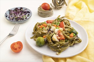 Tagliatelle green spinach pasta with tomato, pea and microgreen sprouts on a white wooden