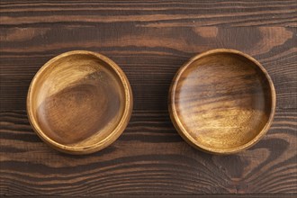 Two empty brown wooden bowl on brown wooden background. Top view, copy space, flat lay