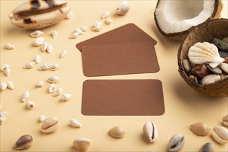 Brown paper business card with coconut and seashells on orange pastel background. Side view, copy