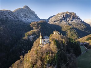 A church on a hill with a view of a castle ruin and wooded mountains in the morning light, St