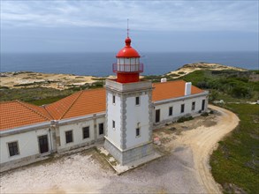 Close-up of a lighthouse and a neighbouring building overlooking the sea under a cloudy sky Aerial