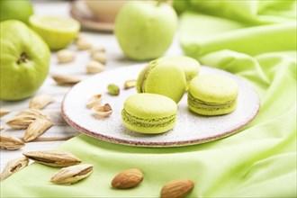 Green macarons or macaroons cakes with cup of coffee on a white wooden background and green linen