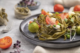 Tagliatelle green spinach pasta with tomato, pea and microgreen sprouts on a gray concrete