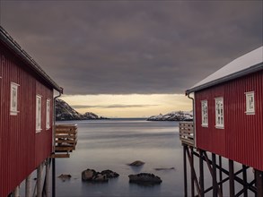 View between two traditional red wooden houses across the fjord to the mountains of the mainland,