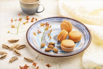 Orange macarons or macaroons cakes with cup of coffee on a white concrete background and linen