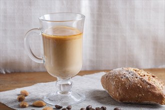 Glass cup of coffee with cream and bun on a wooden background and linen textile. close up, copy