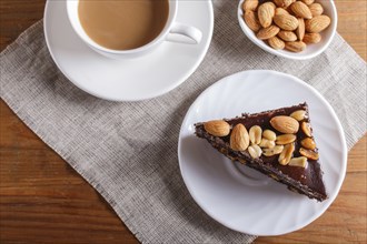 Chocolate cake with caramel, peanuts and almonds on a brown wooden background. cup of coffee, top