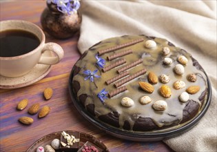 Homemade chocolate brownie cake with caramel cream and almonds with cup of coffee on a colored