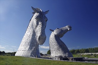 The Kelpies, imposing horse sculptures, tower into the blue sky above an open landscape, Forth and