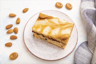 Honey cake with milk cream, caramel, almonds and a cup of coffee on a white concrete background and