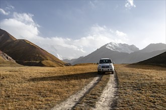 Off-road vehicle on a track between yellow meadows, glaciated high mountain peaks in the