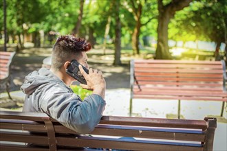 Man sitting on a bench calling on the phone, young man sitting on a bench with cell phone, close up