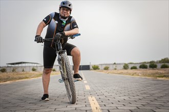 Smiling cyclist on his bike looking at the camera on the road. Chubby male cyclist in sportswear