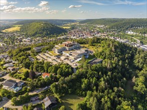 Aerial view of a town in green surroundings, many houses and a large building on a hill, blue