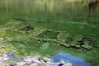 Clear, green water with visible stones and ruins underneath, surrounded by natural landscape,