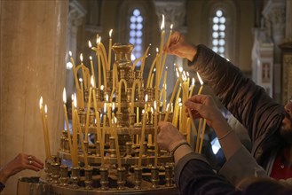 Several hands put burning candles into a candlestick, Greek Orthodox Cathedral of the Annunciation,