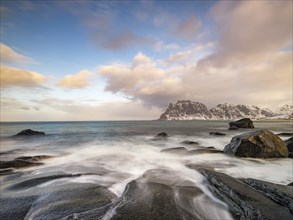 Smoothly polished rocks on Utakleiv beach in a dramatic cloudy atmosphere, snow-capped mountains in