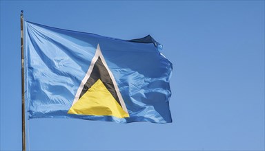 The flag of St Lucia, Caribbean, flutters in the wind, isolated against a blue sky