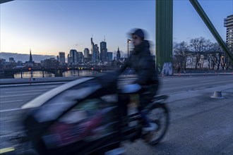 Skyline of the city centre of Frankfurt am Main, cargo bike cyclist on the rafter bridge, dusk,