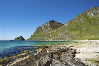 Landscape with sea at the sandy beach of Haukland with the mountain Veggen. Rocks in the foreground