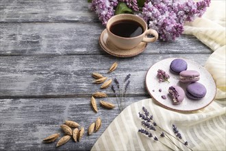 Purple macarons or macaroons cakes with cup of coffee on a gray wooden background and white linen