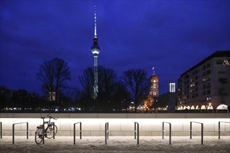 A bicycle stands in an illuminated parking space with a view of the TV tower and the Rotes Rathaus,