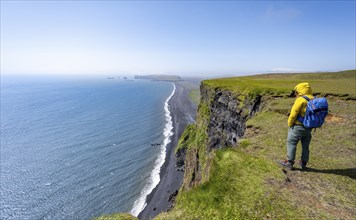 Young man standing on cliff, view from steep cliff over Reynisfjara beach, Black sand beach, Vik,