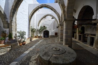 Courtyard of a Greek monastery with white walls, arches and plant pots on a stone floor, Inside the