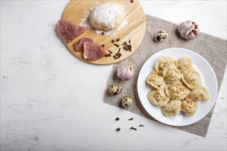 Dumplings on a plate with ingredients (meat, dough, spices) on a linen tablecloth on a white wooden