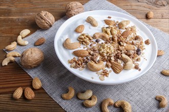 White plate with greek yogurt granola, almond, cashew, walnuts on brown wooden background. close up