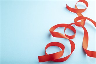 Red coral ribbon on a blue pastel background. Celebration concept. Side view, copy space