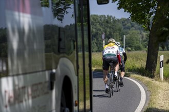 Road cyclist on a country road followed by a local bus that cannot overtake the cyclists on a bend