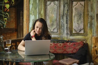 Amidst the rustic charm of a vintage cafe, an adult woman focuses on a laptop, blending modern