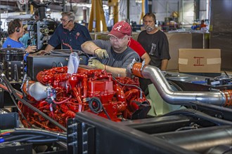 Worker installing a Cumins ISL diesel engine on chassis at Tiffin Motorhomes factory in Red Bay,