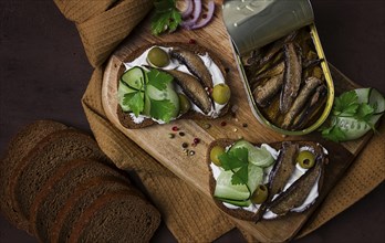 Sandwiches, black bread with sprats, cream cheese, cucumbers, on a cutting board, top view,