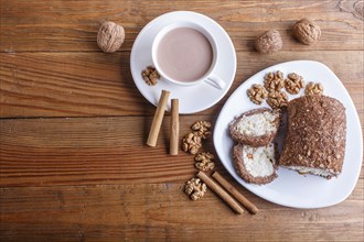 Roll cake with curd and walnuts isolated on brown wooden background. top view, copy space