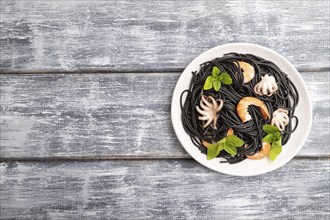 Black cuttlefish ink pasta with shrimps or prawns and small octopuses on gray wooden background.